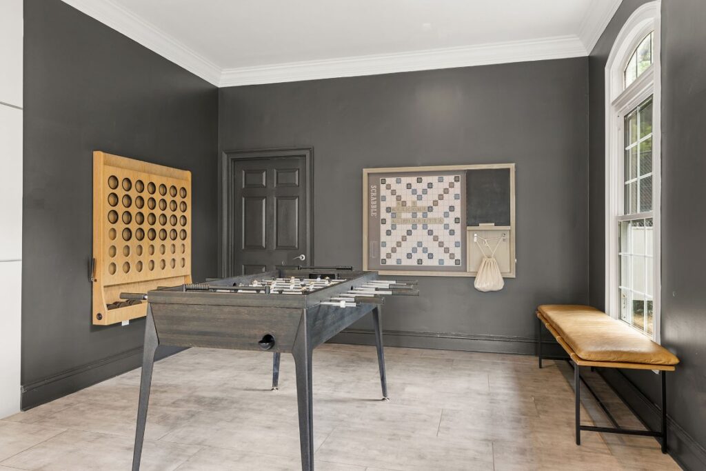 A game room featuring a foosball table, a wall-mounted giant connect four game, and a large Scrabble board on the wall, with a bench seat near the window.