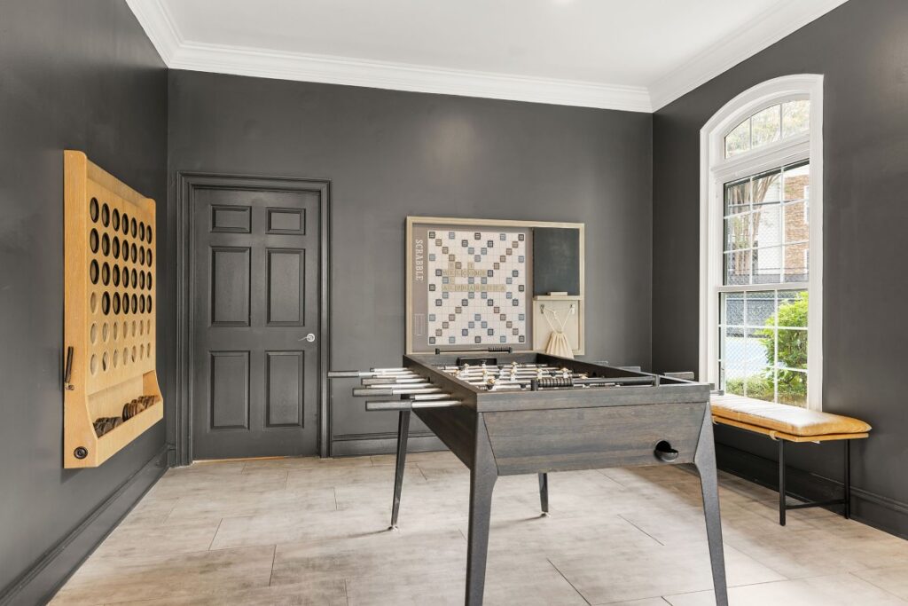 A game room with a foosball table in the center, a wall-mounted oversized Connect Four game, and a Scrabble board mounted on the wall.