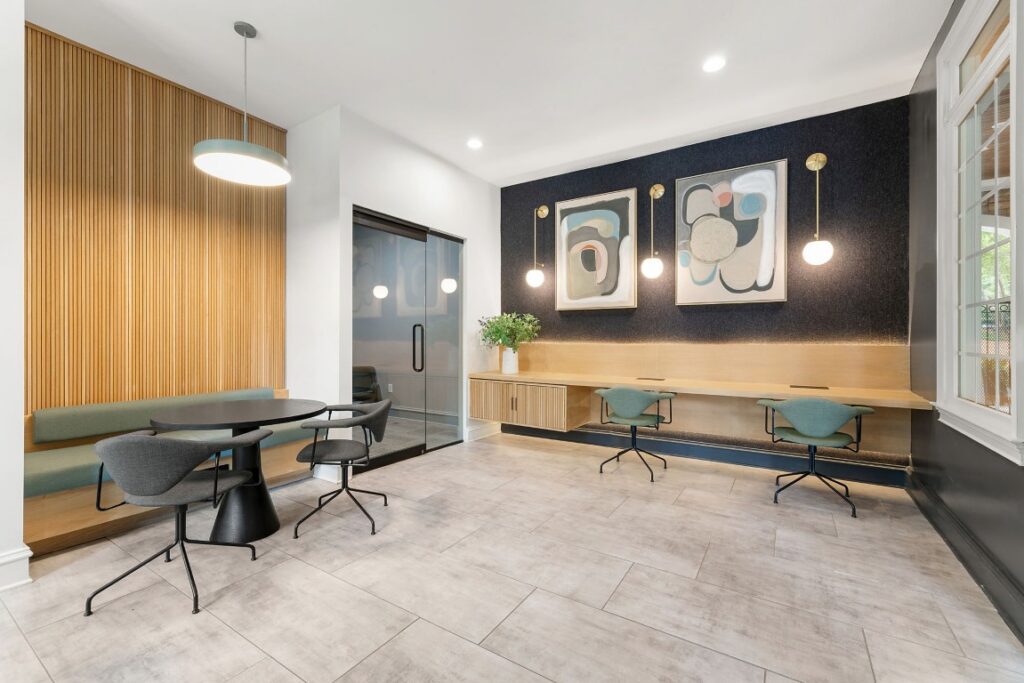 Modern office lounge with a round table, a built-in wooden desk, and green swivel chairs against a dark feature wall with abstract art.