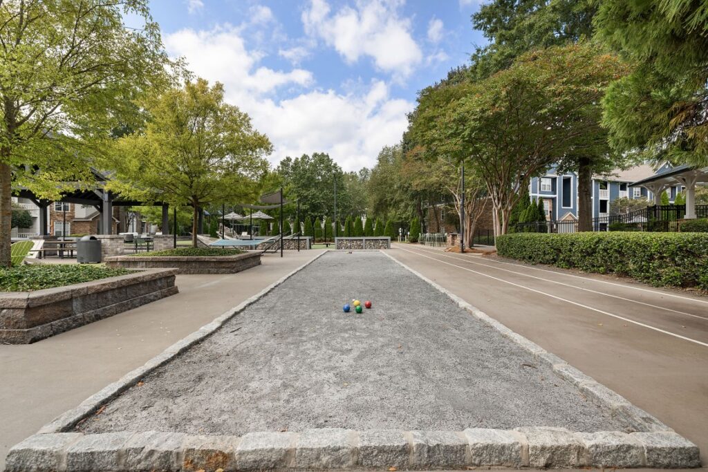 A gravel bocce ball court sits between walkways in a residential courtyard, with four colored bocce balls resting in the center.