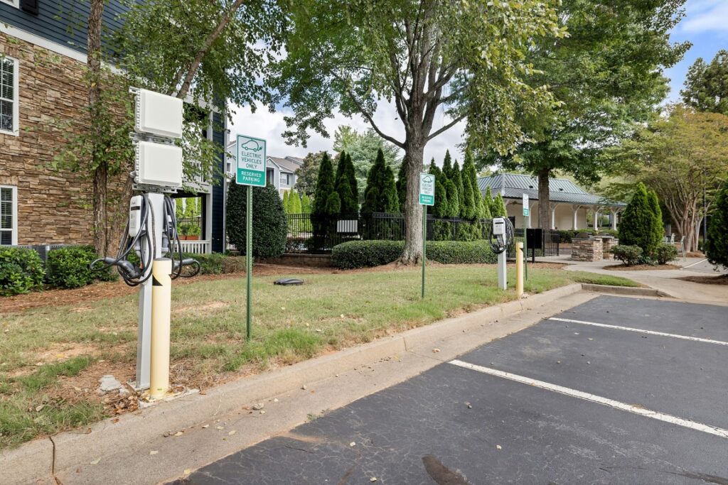 Two electric vehicle charging stations with reserved parking signs in a parking lot next to a grassy area and apartment buildings.