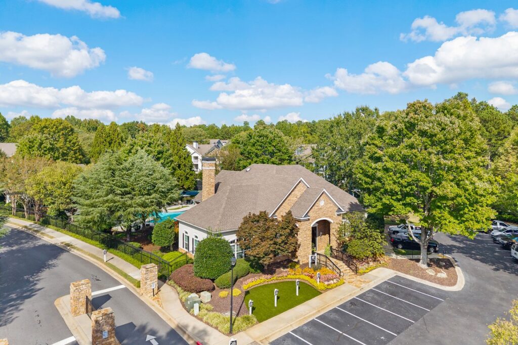 Aerial view of a residential leasing office building with a surrounding parking lot and a swimming pool in the background.