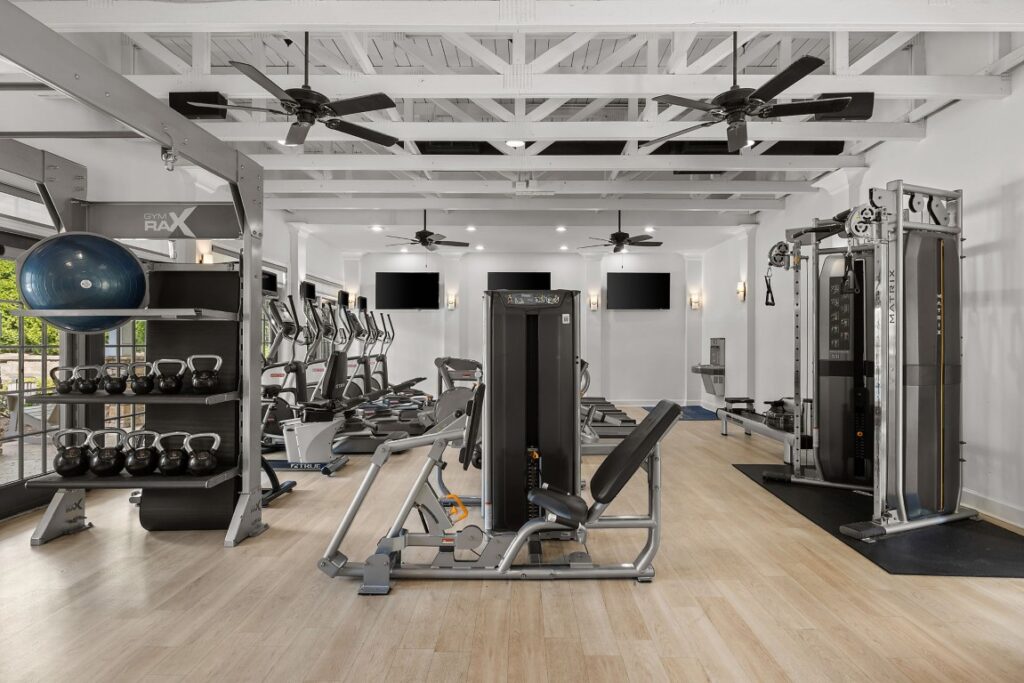A gym interior featuring a variety of weight machines, treadmills, a rack of kettlebells, and a blue exercise ball.