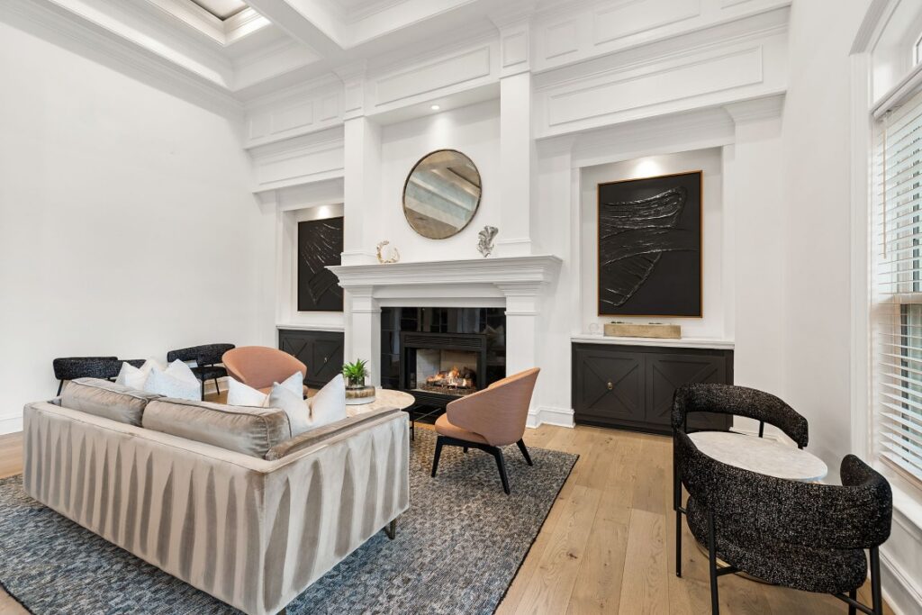 A living room with a white fireplace, two pink armchairs, a large velvet sofa, and black built-in cabinets featuring modern art.