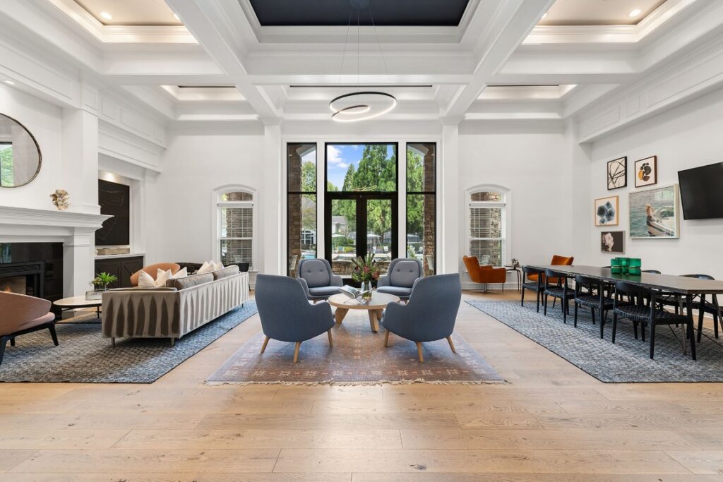 A bright, open-concept living and dining room with a coffered ceiling, featuring a seating area with blue armchairs and a dining table with black chairs.