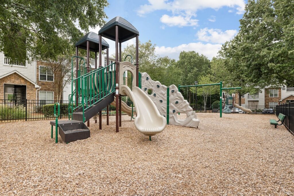 Playground with a slide, climbing wall, and stairs on a wood-chip ground covering.