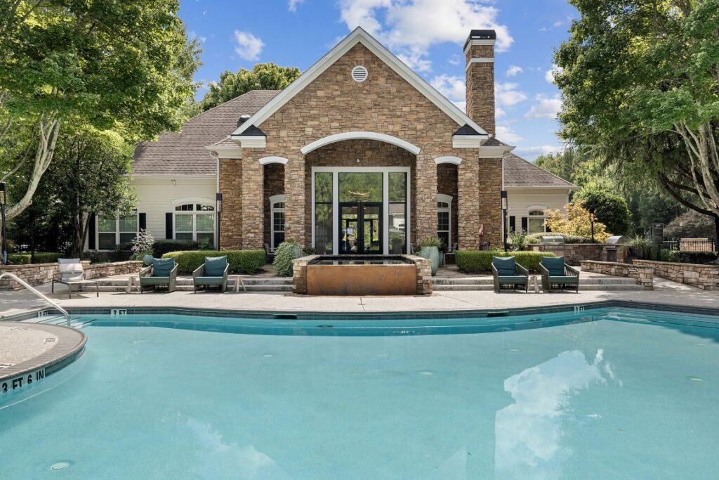 A stone clubhouse with a large arched entrance overlooks a swimming pool surrounded by lounge chairs.