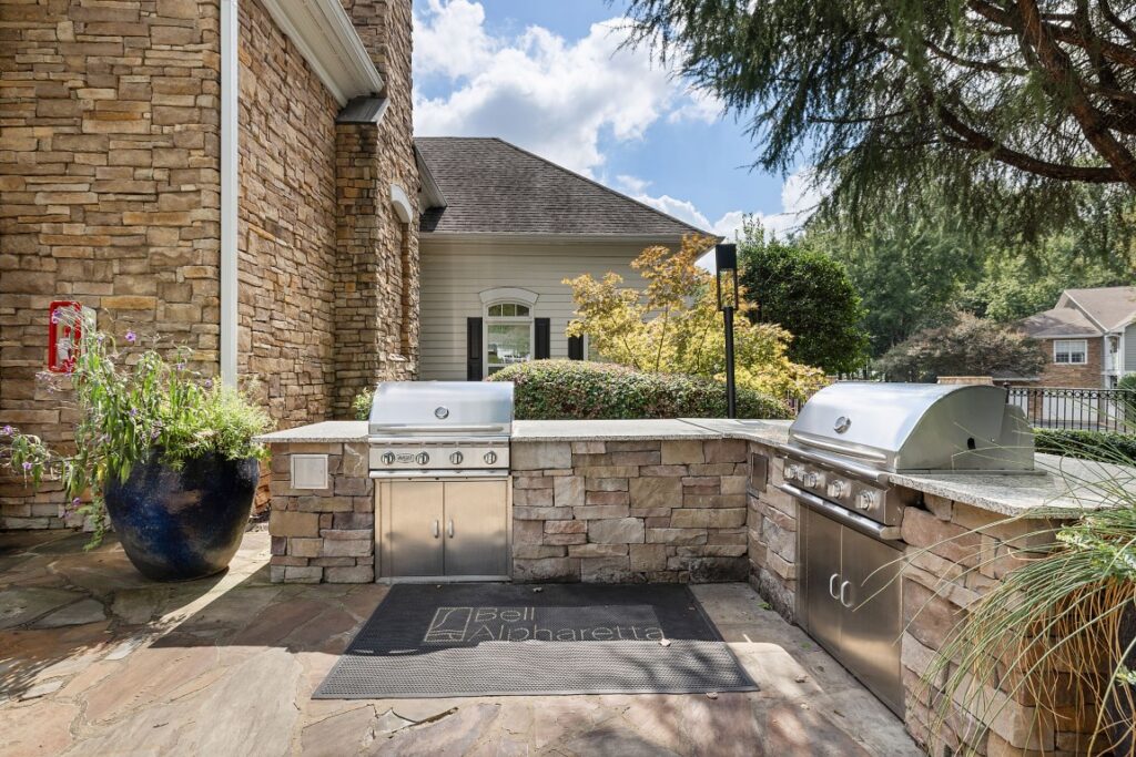 An outdoor kitchen area with two stainless steel grills built into a stone island, situated on a stone patio.