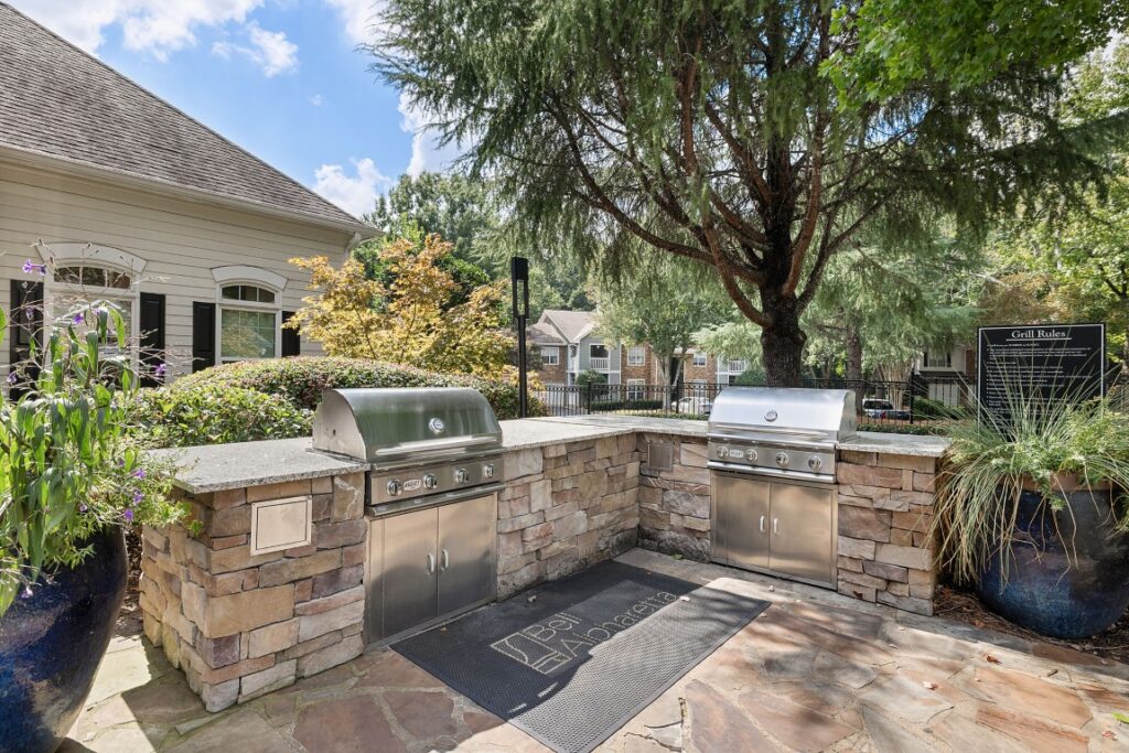 An outdoor grilling station with two stainless steel grills set into a stone counter on a flagstone patio.