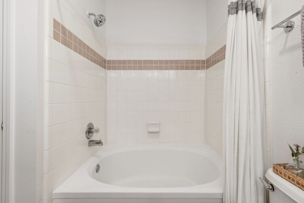 Bathtub and shower combination with white square tiles and a tan accent stripe.