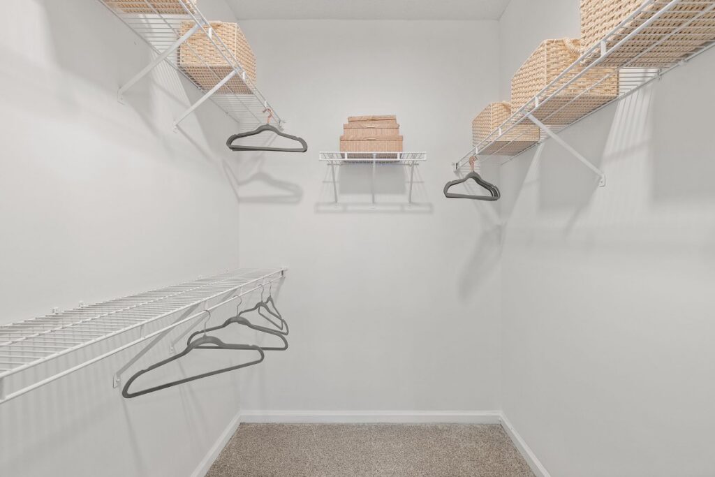 Empty walk-in closet with wire shelving, hanging clothes hangers, and woven storage baskets.
