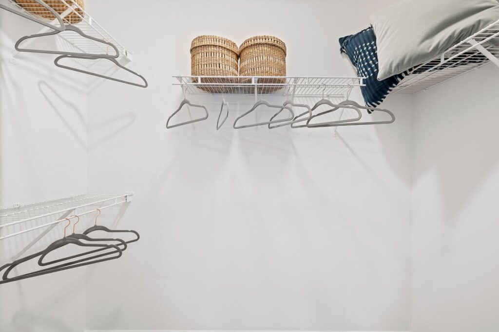 White wire closet shelving with hanging clothes hangers, two wicker baskets, and a pillow.
