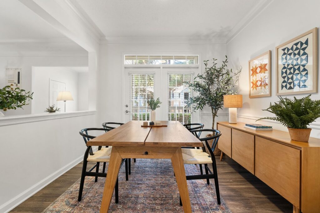 Dining room with a wooden table, four black chairs with woven seats, a wooden sideboard, and geometric wall art.